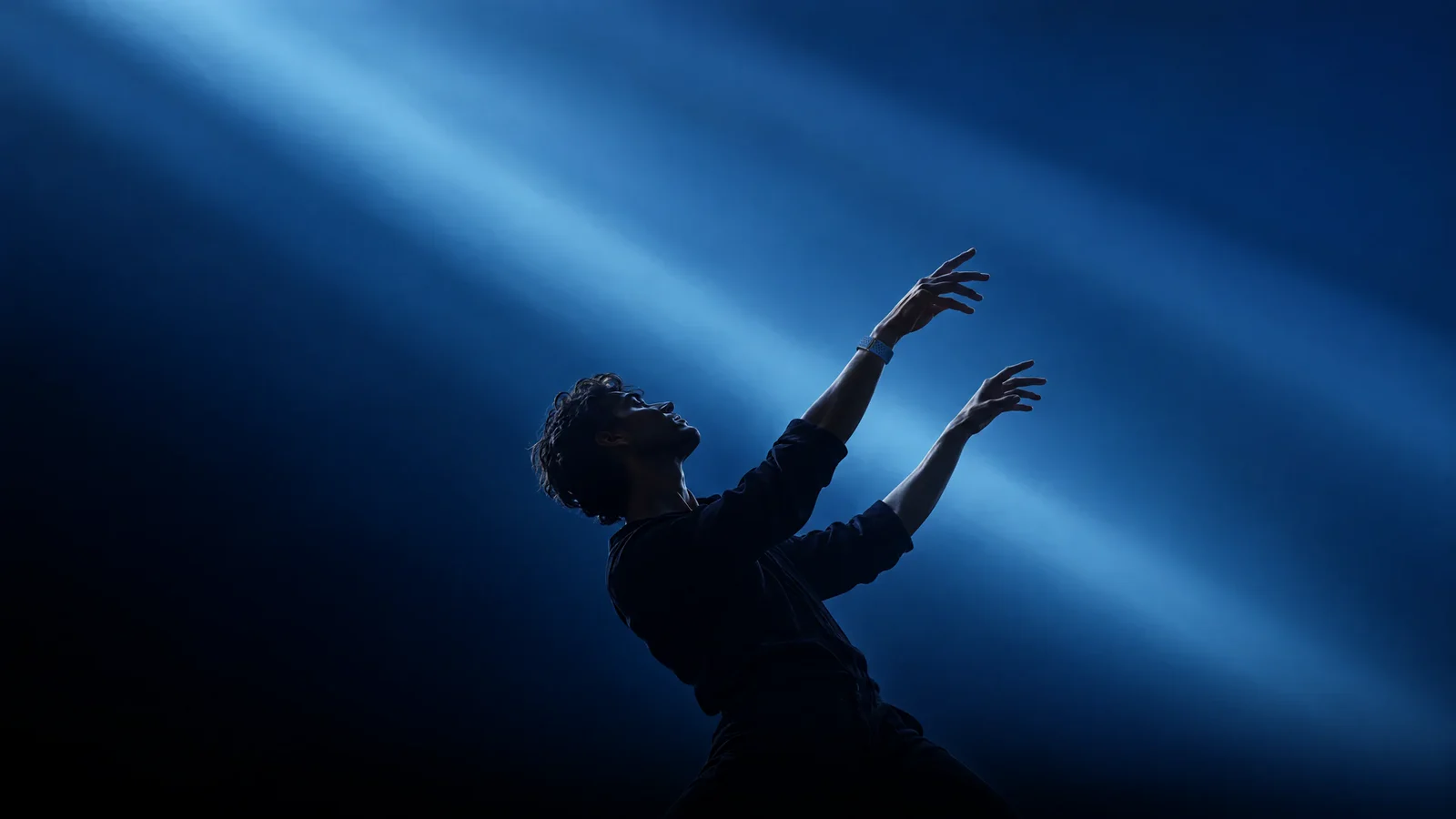 A man leaning back with both arms raised through beams of blue light, wearing the PhenomeTech Band in Harbour