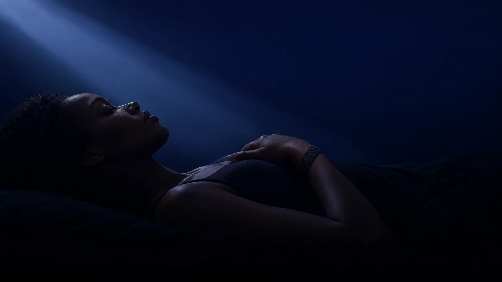 A woman asleep in a beam of moonlight, one hand on her chest, wearing the PhenomeTech Band in Onyx
